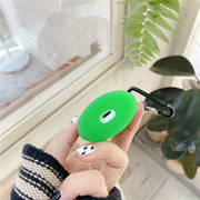 Hand holding a green tea drink earphone case with a clip, against a window backdrop and green plants.