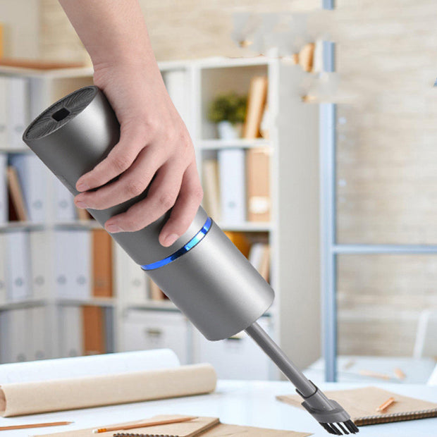 Hand holding a Mini car vacuum cleaner HK6033 in a modern workspace setting.