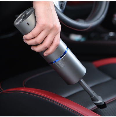 Hand holding a mini car vacuum cleaner, cleaning the leather seat of a car interior.